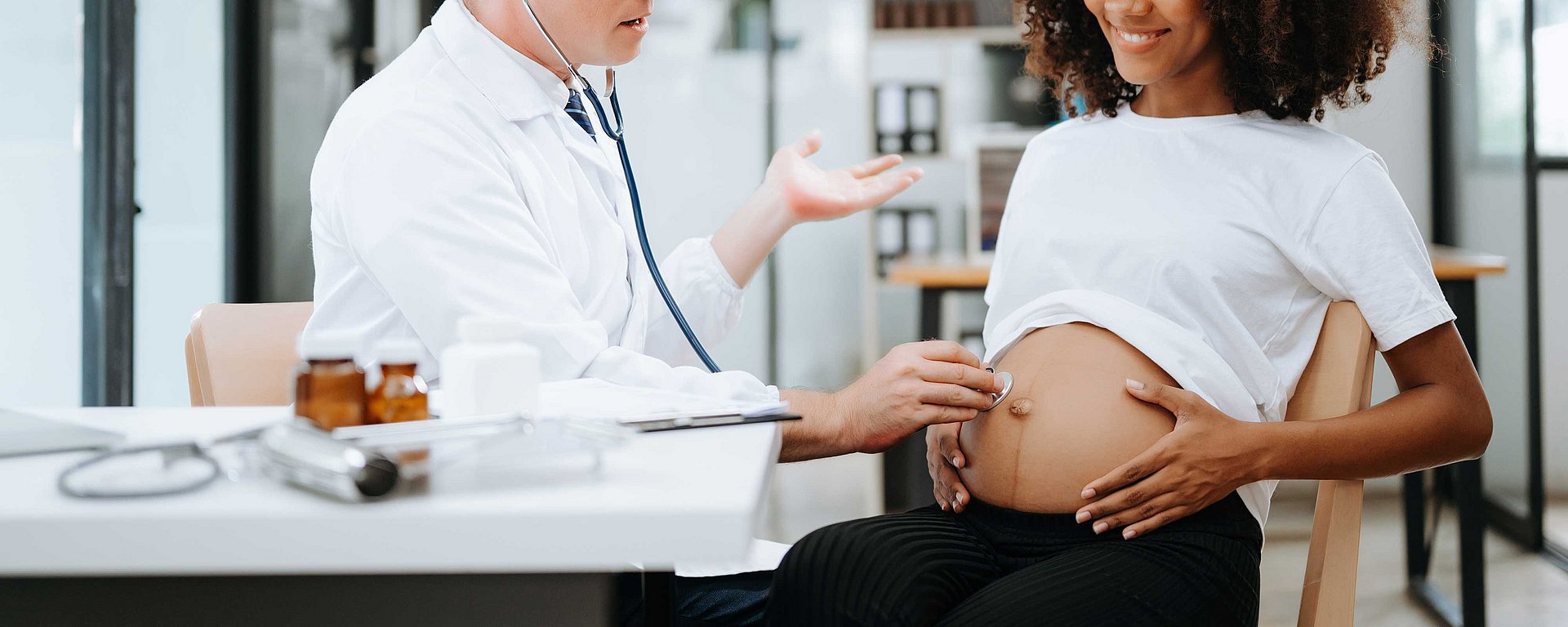 Ein Arzt untersucht bei einer Schwangerschaftsvorsorgeuntersuchung mit einem Stethoskop den Bauch einer Schwangeren.