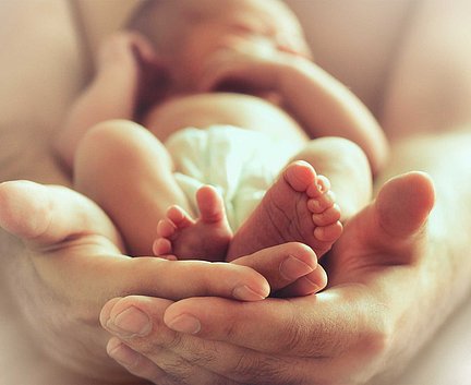 Ein Neugeborenes in einer Windel, das sanft in den Händen eines Erwachsenen ruht, wobei der Fokus auf den winzigen Füßchen des Babys liegt.