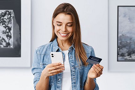 Lächelnde Frau, die ein Smartphone und eine Kreditkarte in der Hand hält und offenbar eine Online-Zahlung vornimmt.