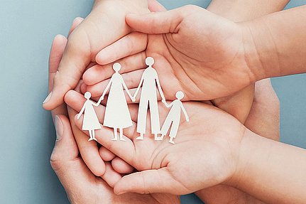 Hände, die Papierausschnitte einer vierköpfigen Familie halten, die Schutz, Fürsorge und Unterstützung symbolisieren.