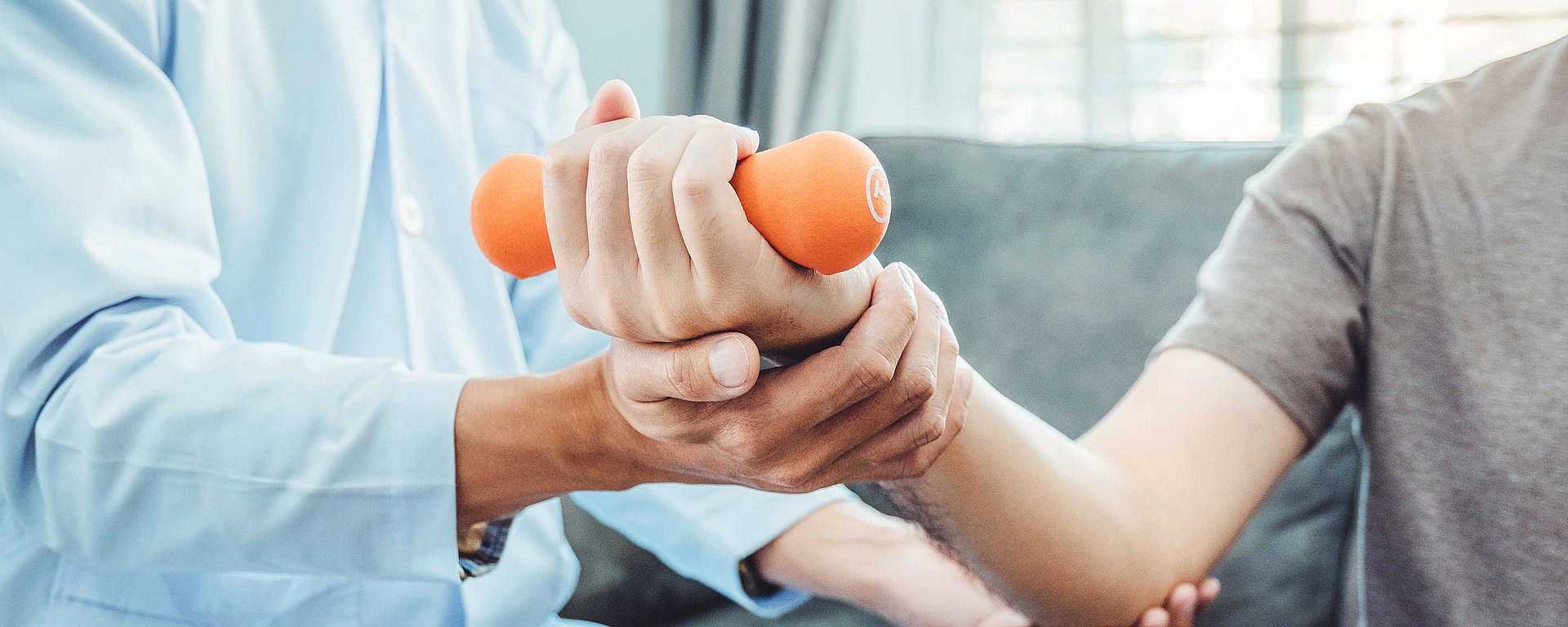 Ein Therapeut hilft einer Person dabei, während einer Physiotherapie-Sitzung eine orangefarbene Hantel zu heben.
