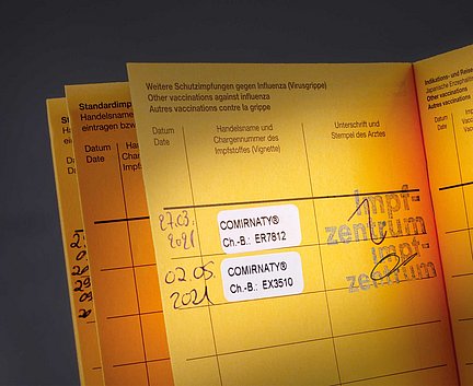 Ein gelber Impfpass mit zwei Comirnaty-COVID-19-Impfaufklebern und ärztlichen Stempeln.