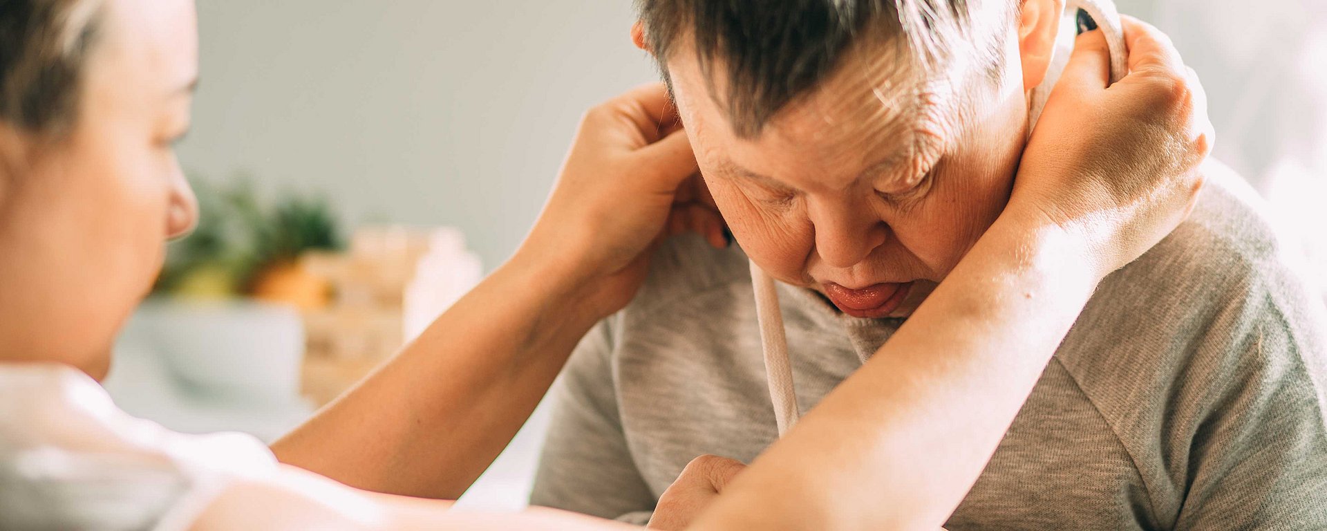 Eine Pflegekraft hilft einem Mann mit Down-Syndrom dabei, die Kordeln seines Kapuzenpullovers in einem Raum zuzubinden.