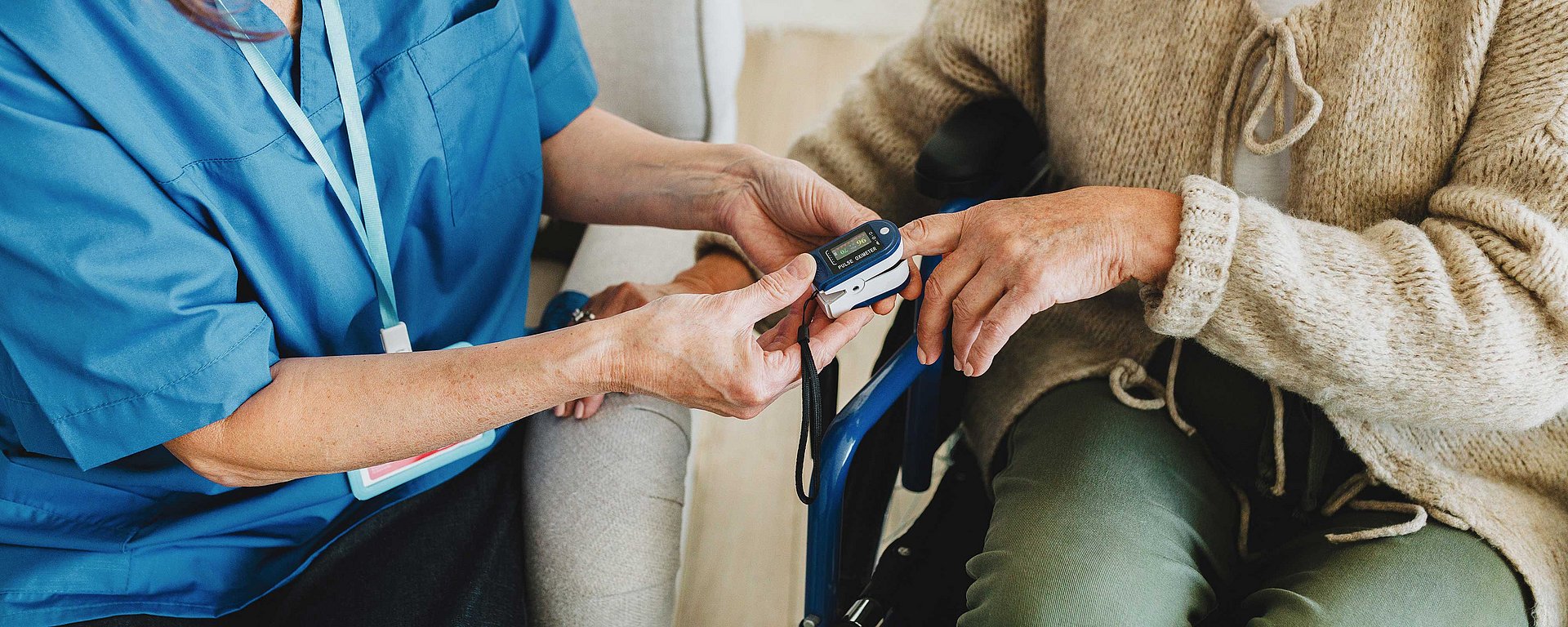 Eine Pflegekraft misst den Blutsauerstoffgehalt einer sitzenden Person mit einem Fingerspitzen-Pulsoximeter.