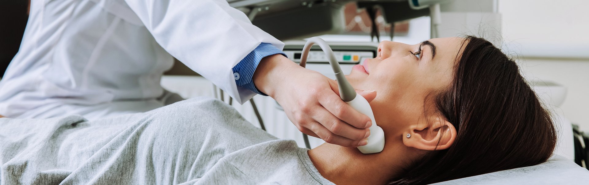 Ein Arzt hält ein Echogerät zweck Tumorbekämpfung an den Hals einer jungen Patientin.