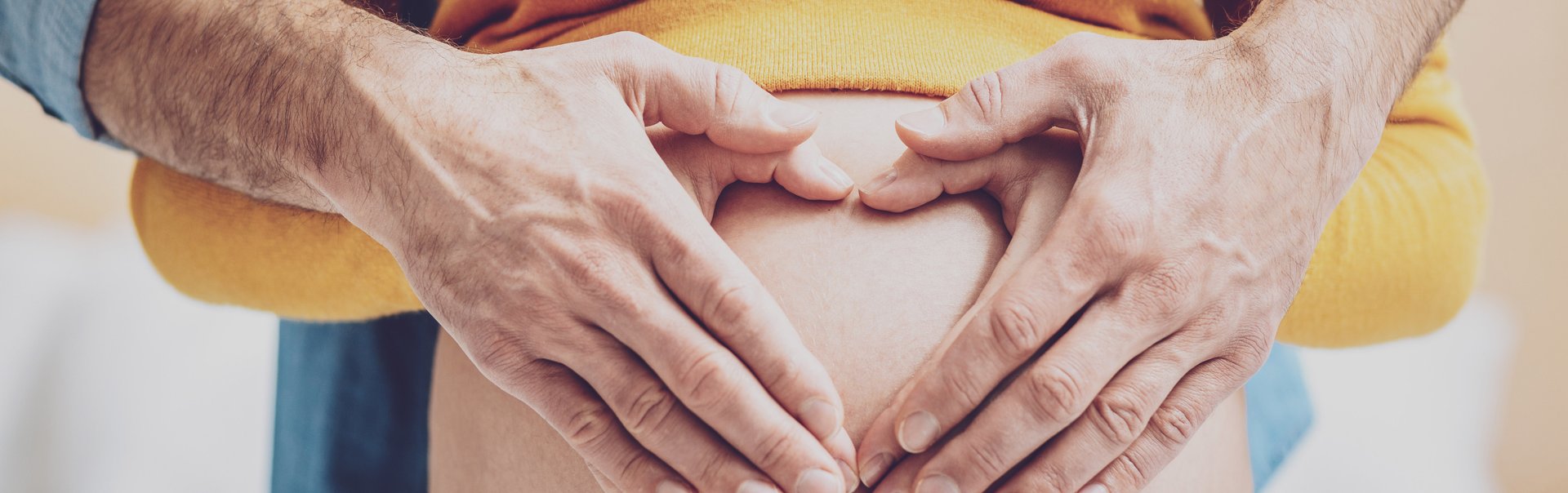 Die Hände von Mann und Frau formen auf einem schwangeren Bauch ein Herz.