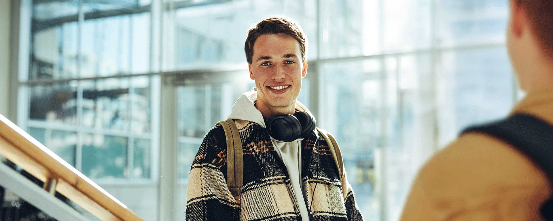 Ein junger Mann mit Kopfhörern um den Hals, der in einem Raum lächelt und sich mit einer anderen Person unterhält.