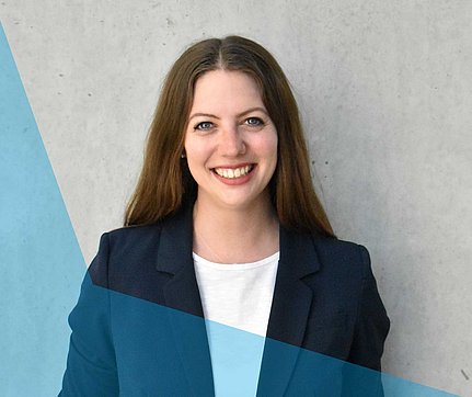 Lächelnde Frau mit langen braunen Haaren in einem Blazer, die vor einem hellgrauen Hintergrund mit blauen Grafiken steht.