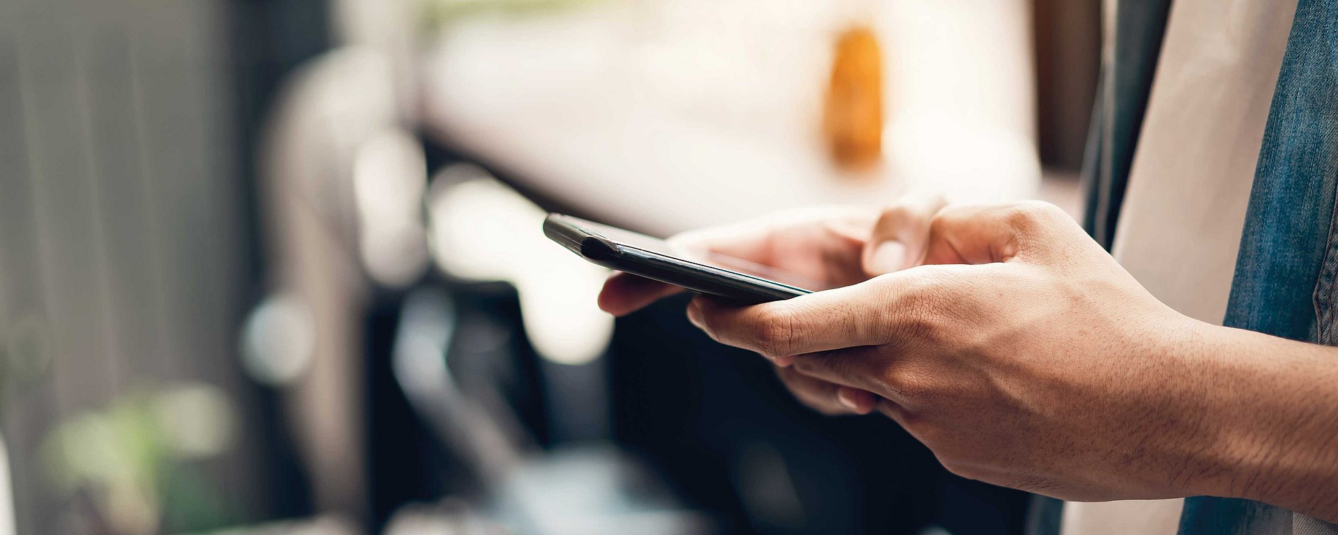 Nahaufnahme der Hände einer Person, die in einem Innenraum ein Smartphone in der Hand hält und benutzt.