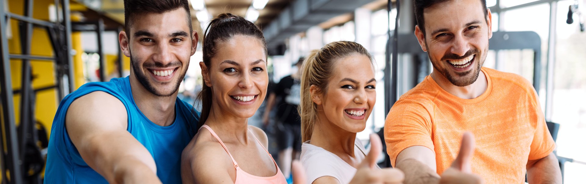 Vier junge Erwachsene stehen lächelnd in einem Fitnessstudio.