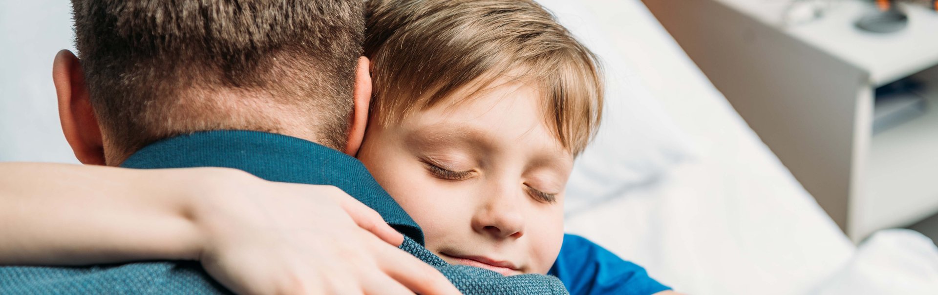 Junge im Krankenhaus umarmt seinen Vater auf dem Krankenbett.