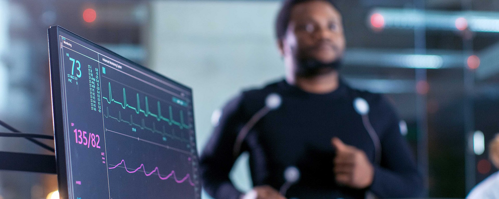 Ein Mann läuft auf einem Laufband, während seine Herzfrequenz und sein EKG auf einem Bildschirm in der Nähe angezeigt werden.