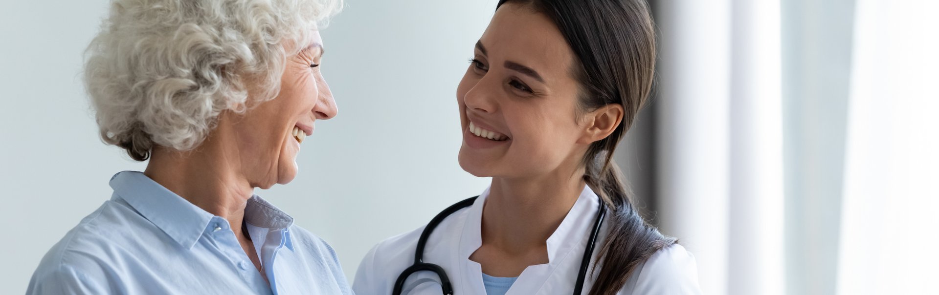 Eine junge Ärztin lächelt eine ältere Patientin an.