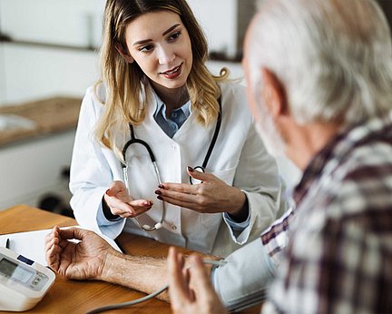 Ein Arzt unterhält sich bei einem Arzttermin mit einem älteren männlichen Patienten, während er dessen Blutdruck misst.