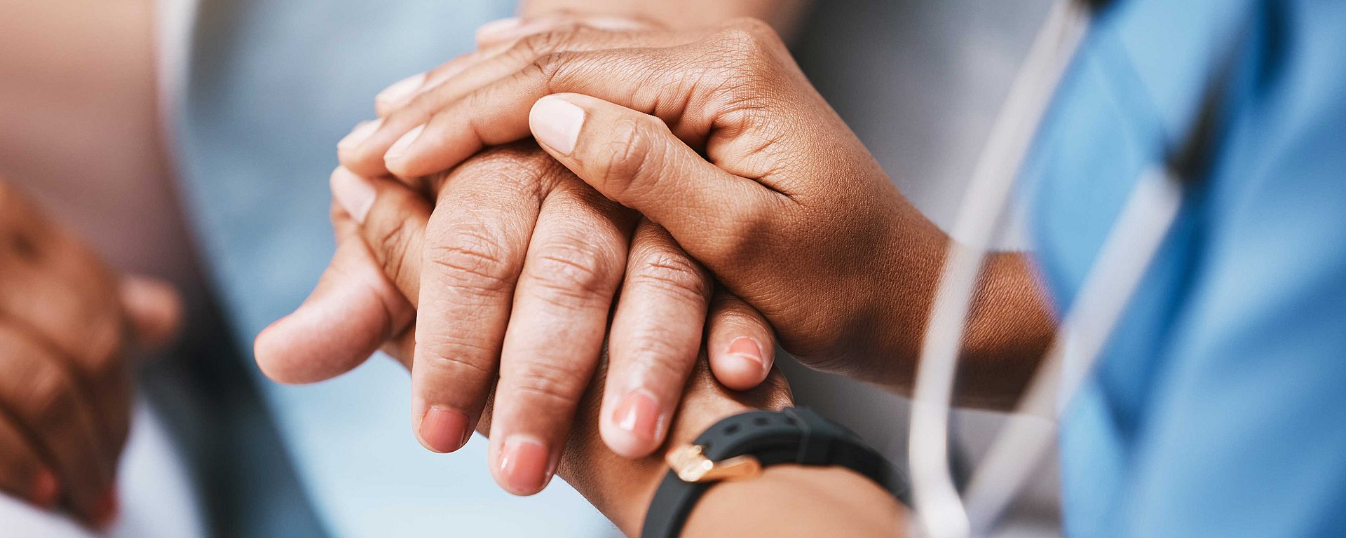 Nahaufnahme der Hand eines Mitarbeiters im Gesundheitswesen, der die Hand eines Patienten sanft und tröstend hält.
