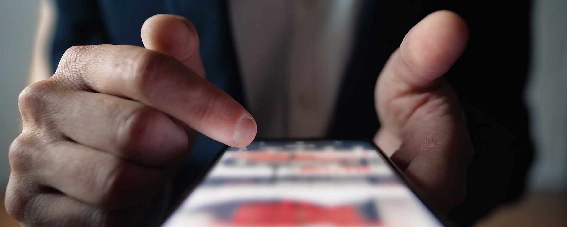 Nahaufnahme der Hand einer Person, die auf den Bildschirm eines Smartphones tippt, wobei der Hintergrund unscharf ist.
