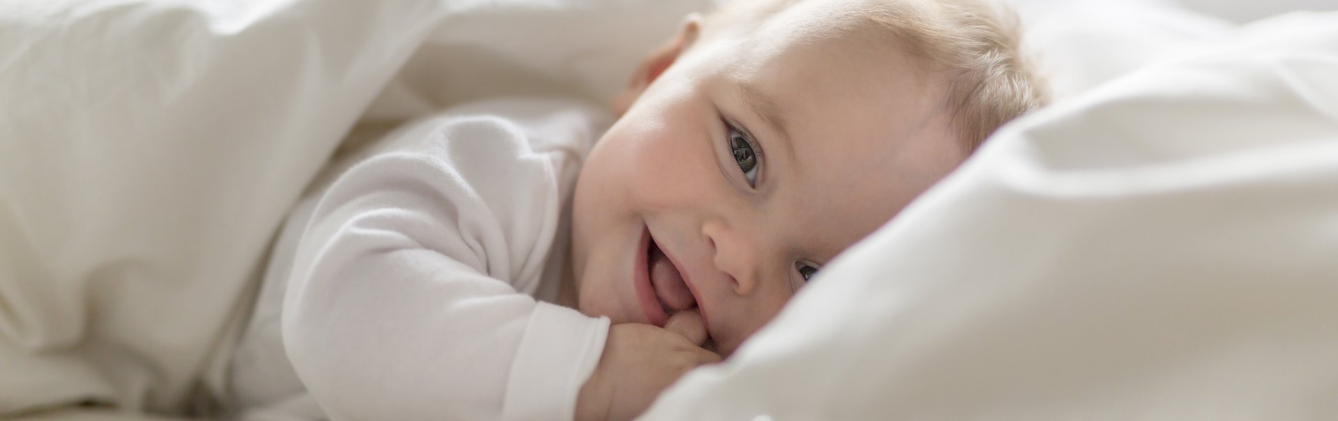 Ein fröhliches Baby liegt in einem Bett.